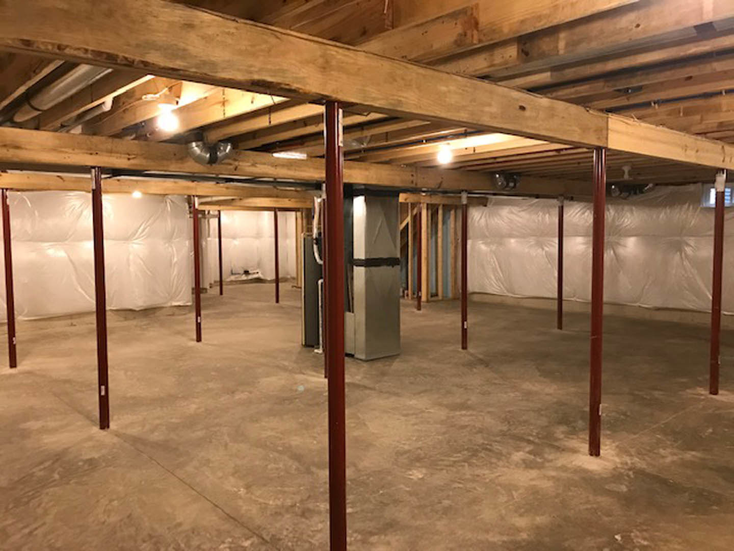 Basement room with exposed wooden ceiling beams, metal support poles, and a metal utility box against the wall.
