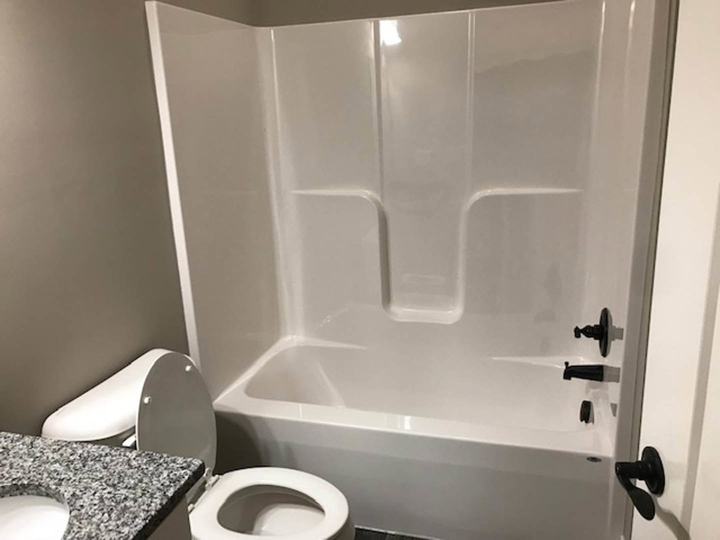 Bathroom featuring a freestanding white bathtub, modern toilet, marble countertop, and light gray tile walls