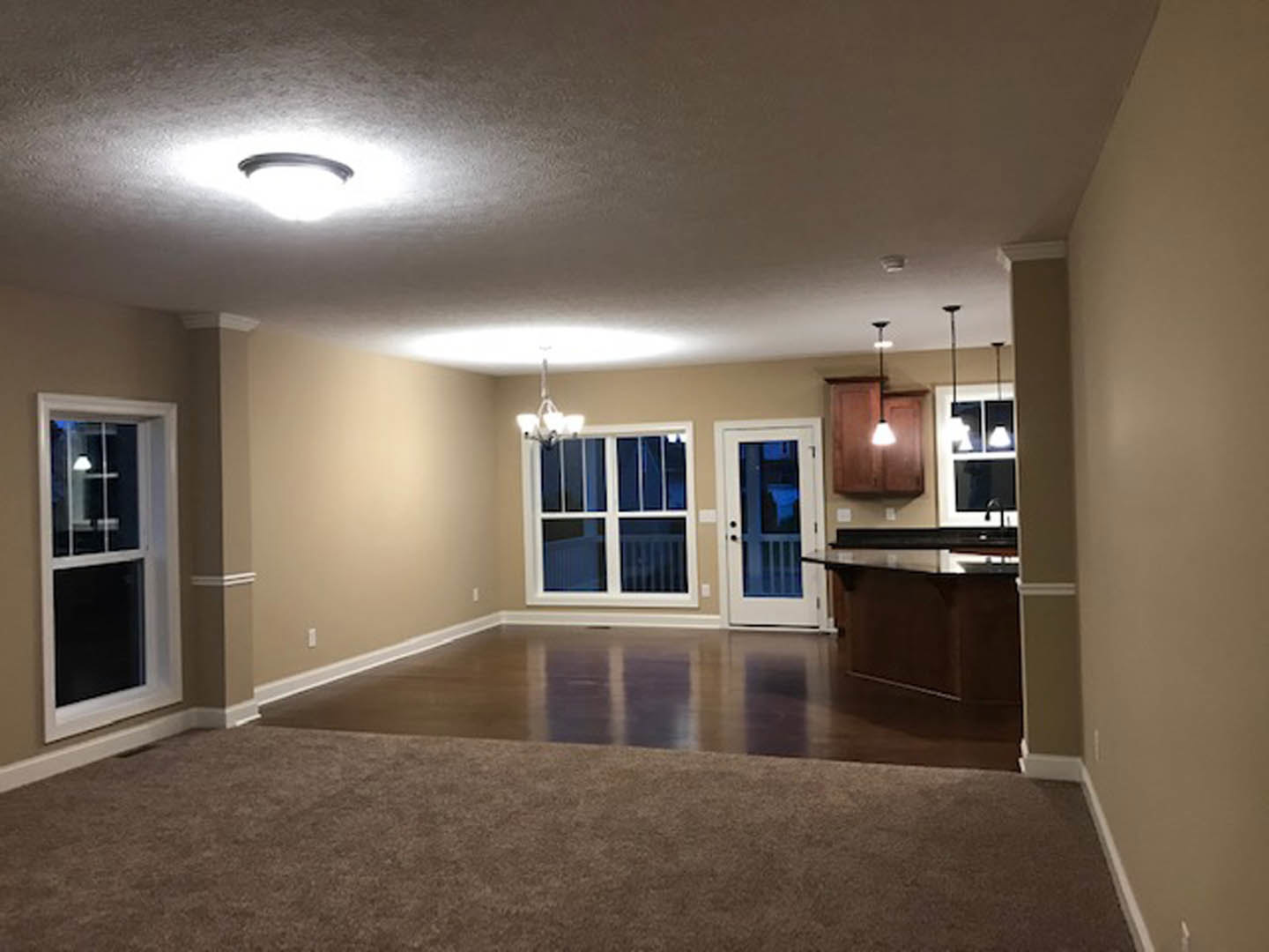 Open concept living room with laminate flooring, white cabinetry kitchen, and adjacent dining area; neutral walls, recessed lighting, and large windows.