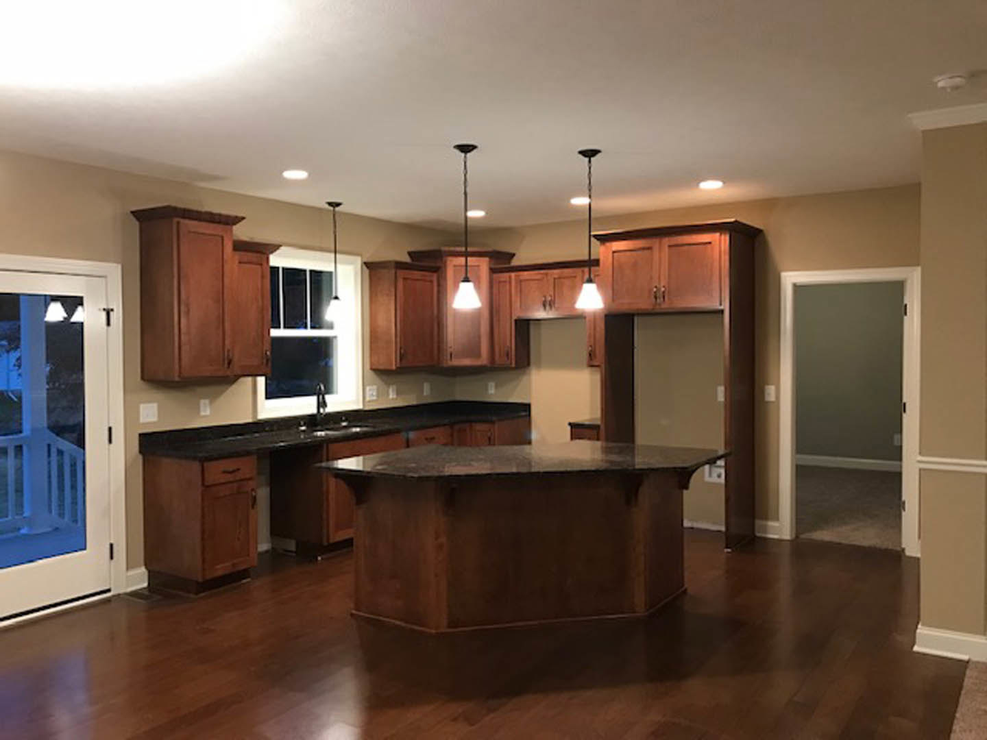 Spacious kitchen featuring a large dark stone island countertop, white cabinetry, stainless steel appliances, wooden flooring, and an open doorway leading to an adjacent room.
