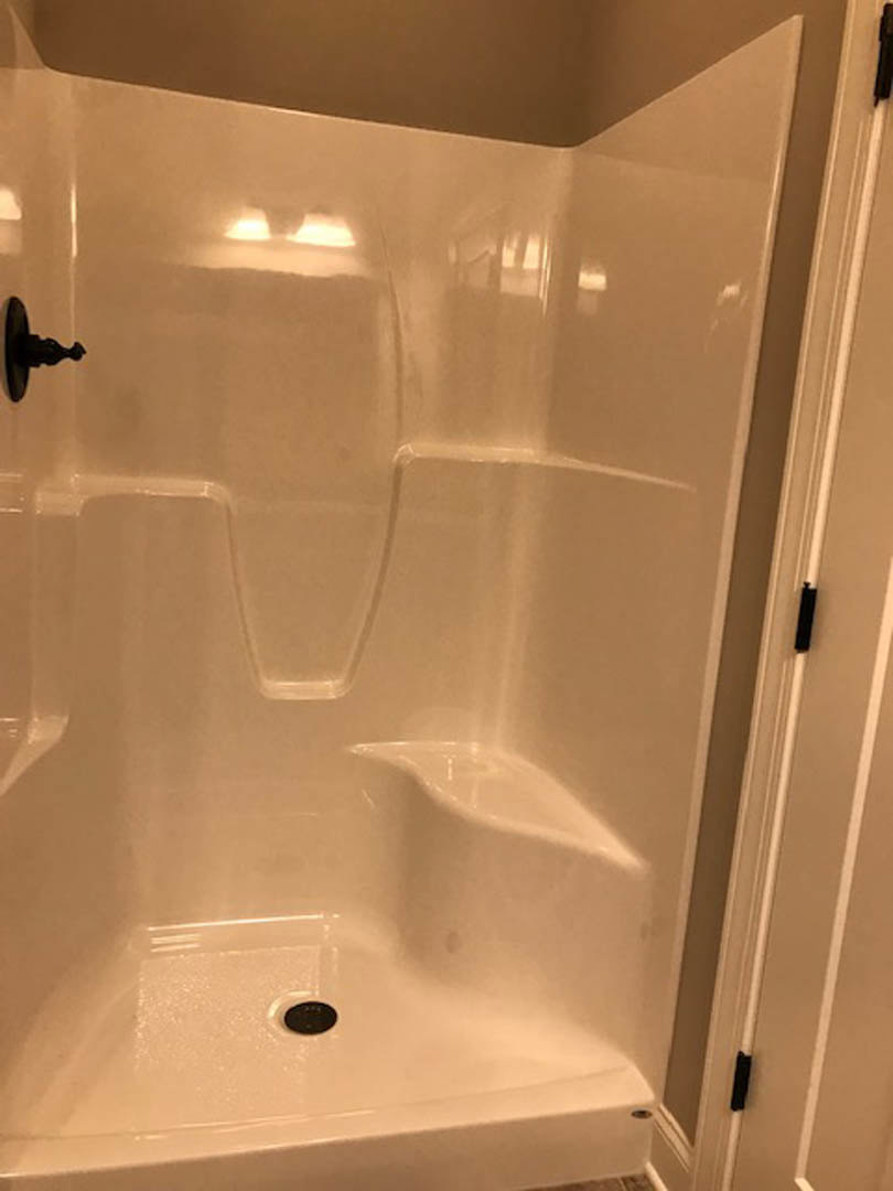 Walk-in shower with chrome shower head, white tile walls, and glass enclosure