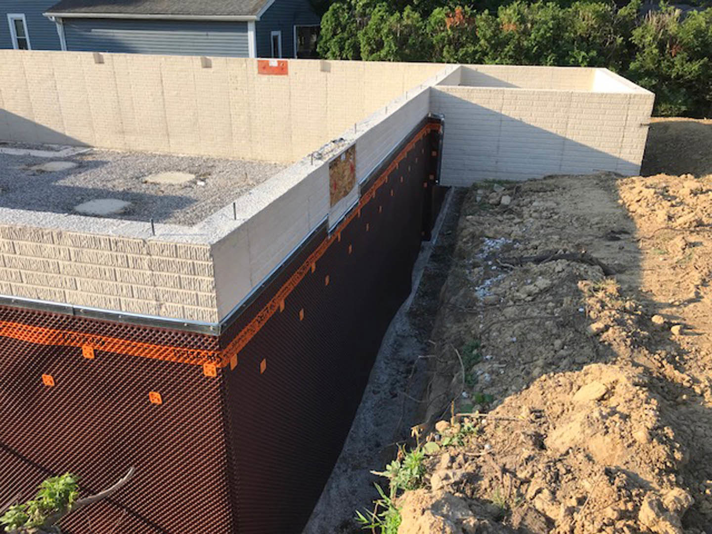 Partially built brick home with orange and white construction tape, surrounded by dirt mound and trees