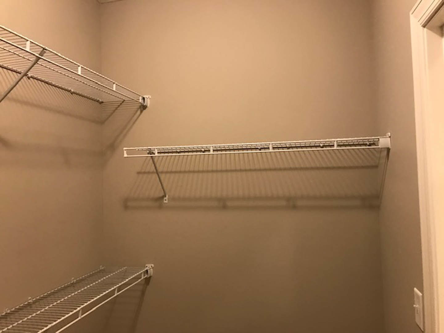 Walk-in closet with white built-in shelves and metal hanging rods, white walls, and a white door knob visible on the side