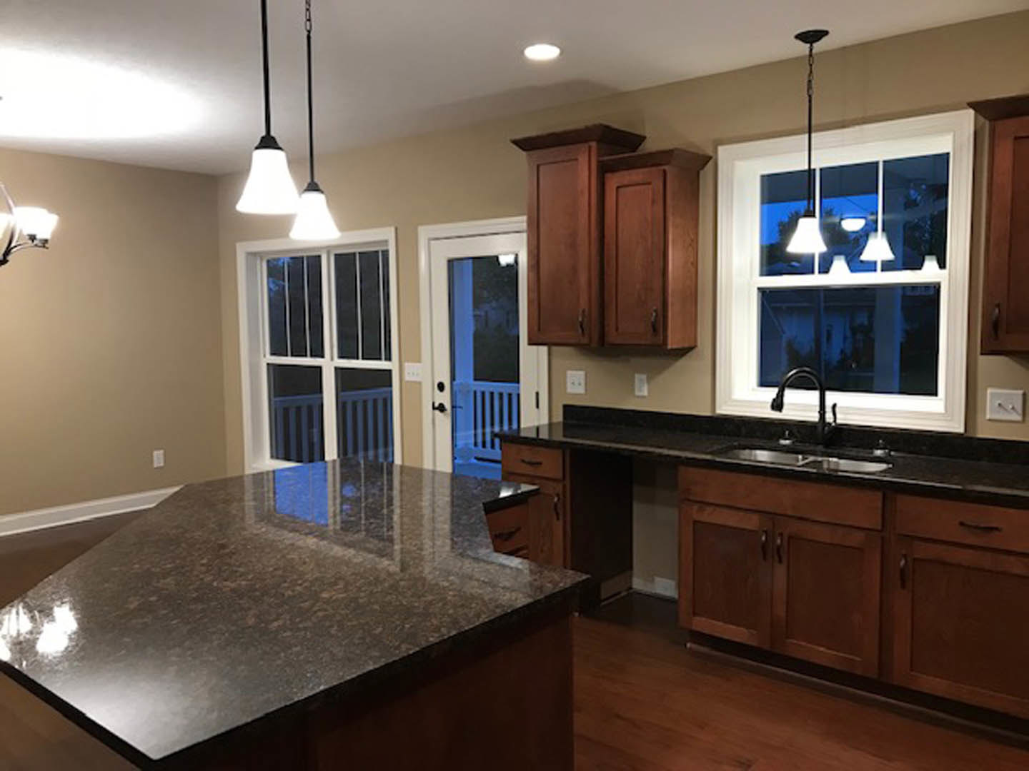 Granite island with white cabinets, stainless steel sink, pendant light fixture, and window reflection on countertop in modern kitchen
