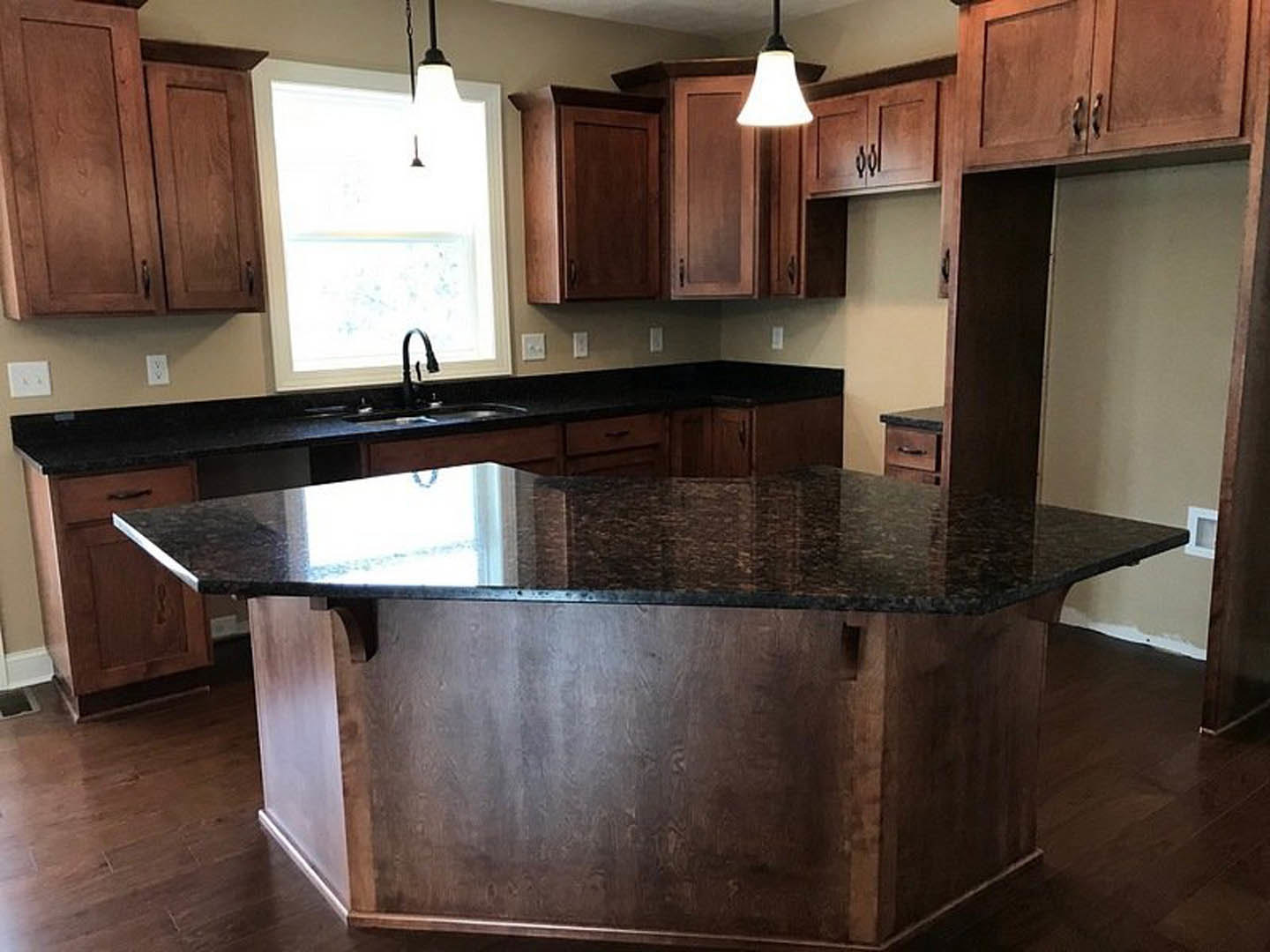 Modern kitchen with matte black countertop, stainless steel faucet, white cabinetry, sunlight streaming through window, and light wood flooring