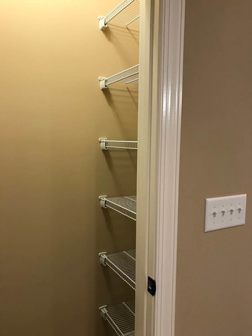 Built-in closet shelves with white wall switches and metal railing, white walls, and close-up view of shelving.