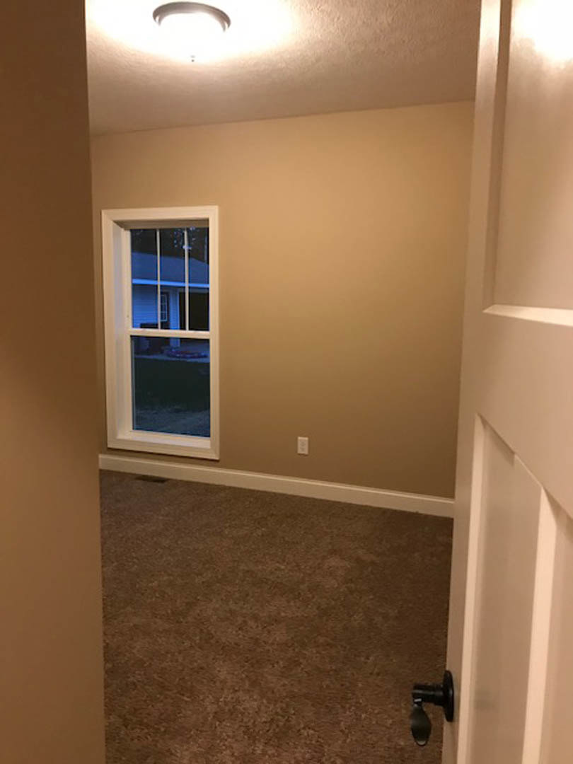 Carpeted bedroom with white walls, large window overlooking neighboring house, black thermostat mounted on wall