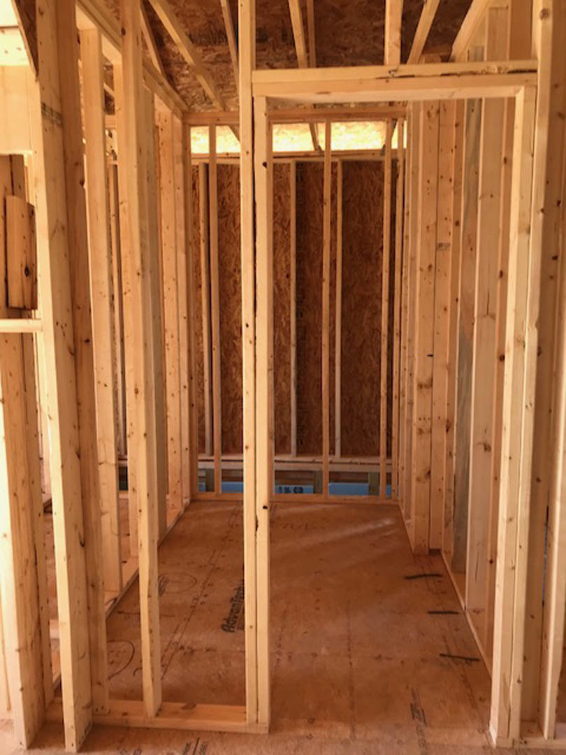 Exposed wood framing with vertical beams and plywood panels inside unfinished room, black electrical box mounted on wall