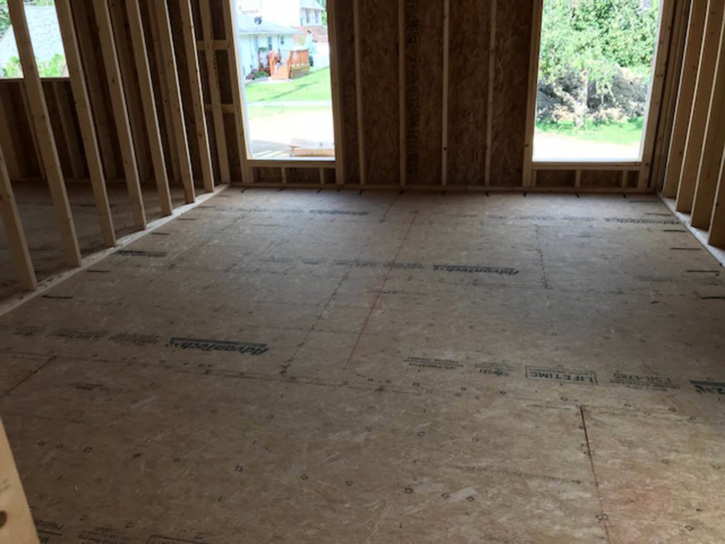 Unfinished room with exposed wooden beams, tile flooring, large window overlooking trees and exterior property
