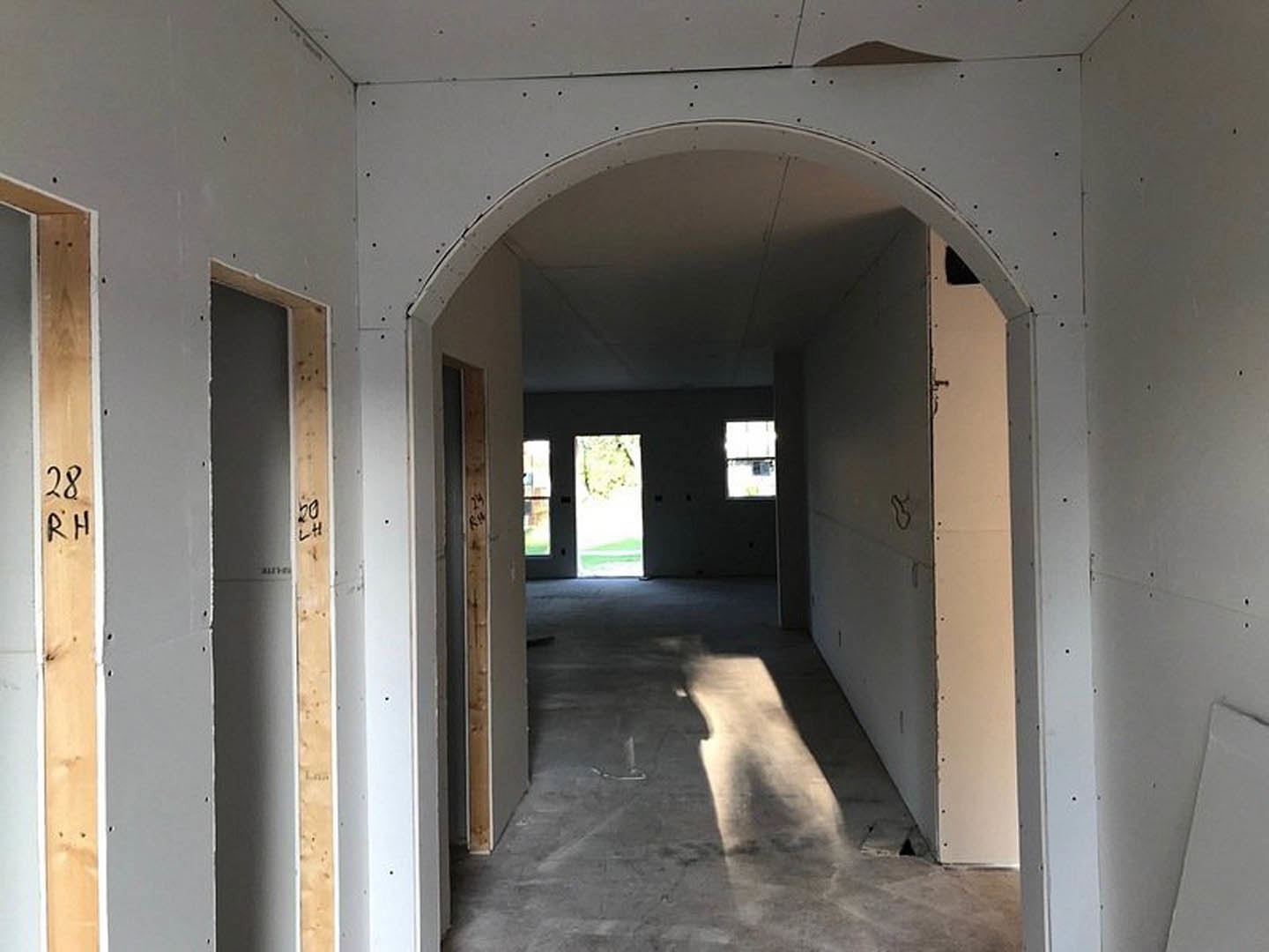 Hallway with arched doorway, windows, light wood flooring, white walls, and a dog sitting near the entrance