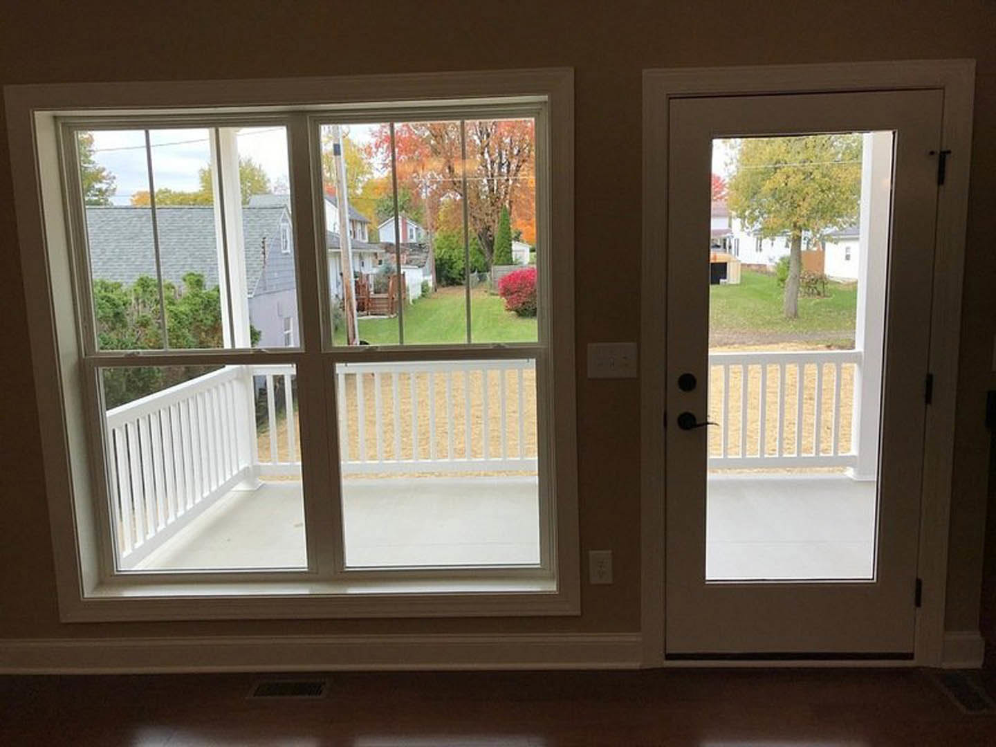 Balcony room with wood flooring, white door, railing, and tree visible outside; light switch on wall and table in foreground