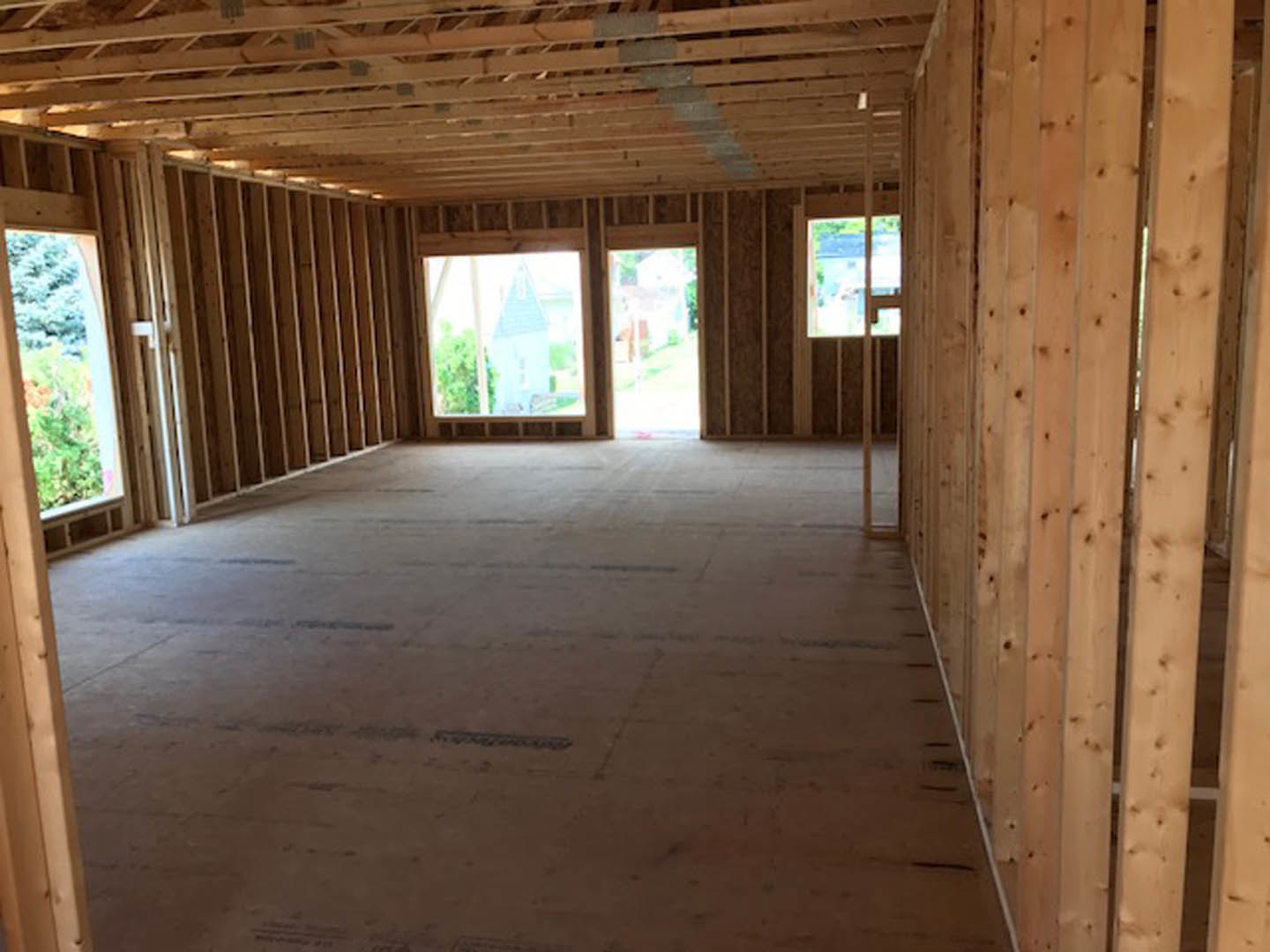 Open room with exposed wood ceiling beams, recessed lighting, large window, and door; hardwood flooring and neutral walls.