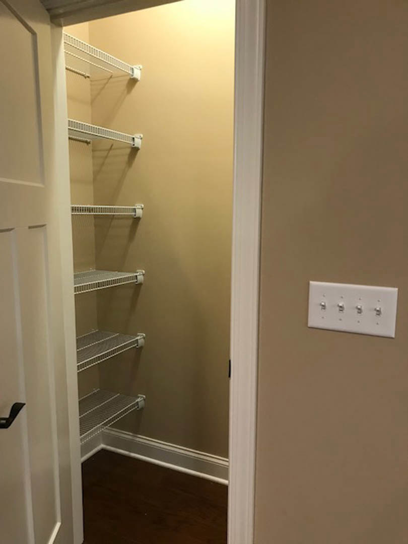 Walk-in closet with white shelving, wood flooring, and a row of light switches on the wall