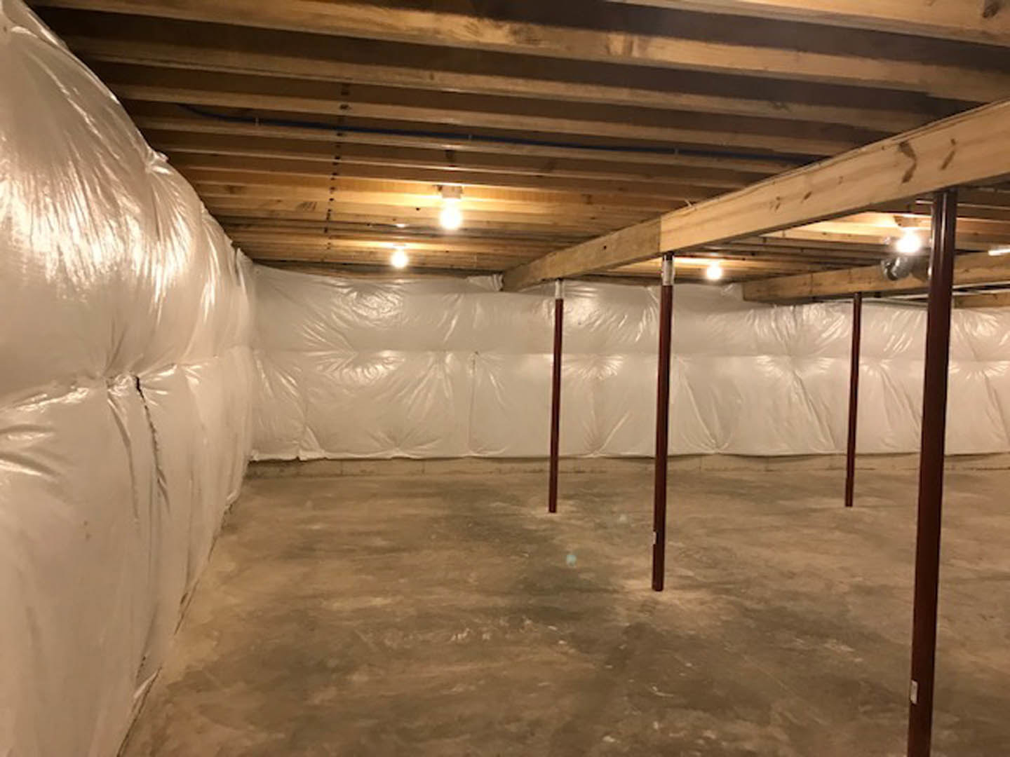 Basement with concrete floor, white plastic wall covering, ceiling lights, and a close-up of a white puffy couch.