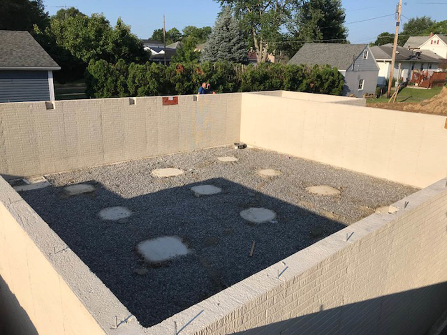 Modern house exterior with concrete foundation, brick walls, flagstone walkway, and leafy tree in landscaped yard