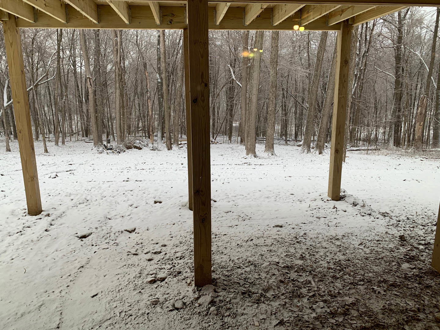 Covered porch with wooden beams and metal brackets, snow-covered ground and wooden posts, view of snowy forest and trees in winter