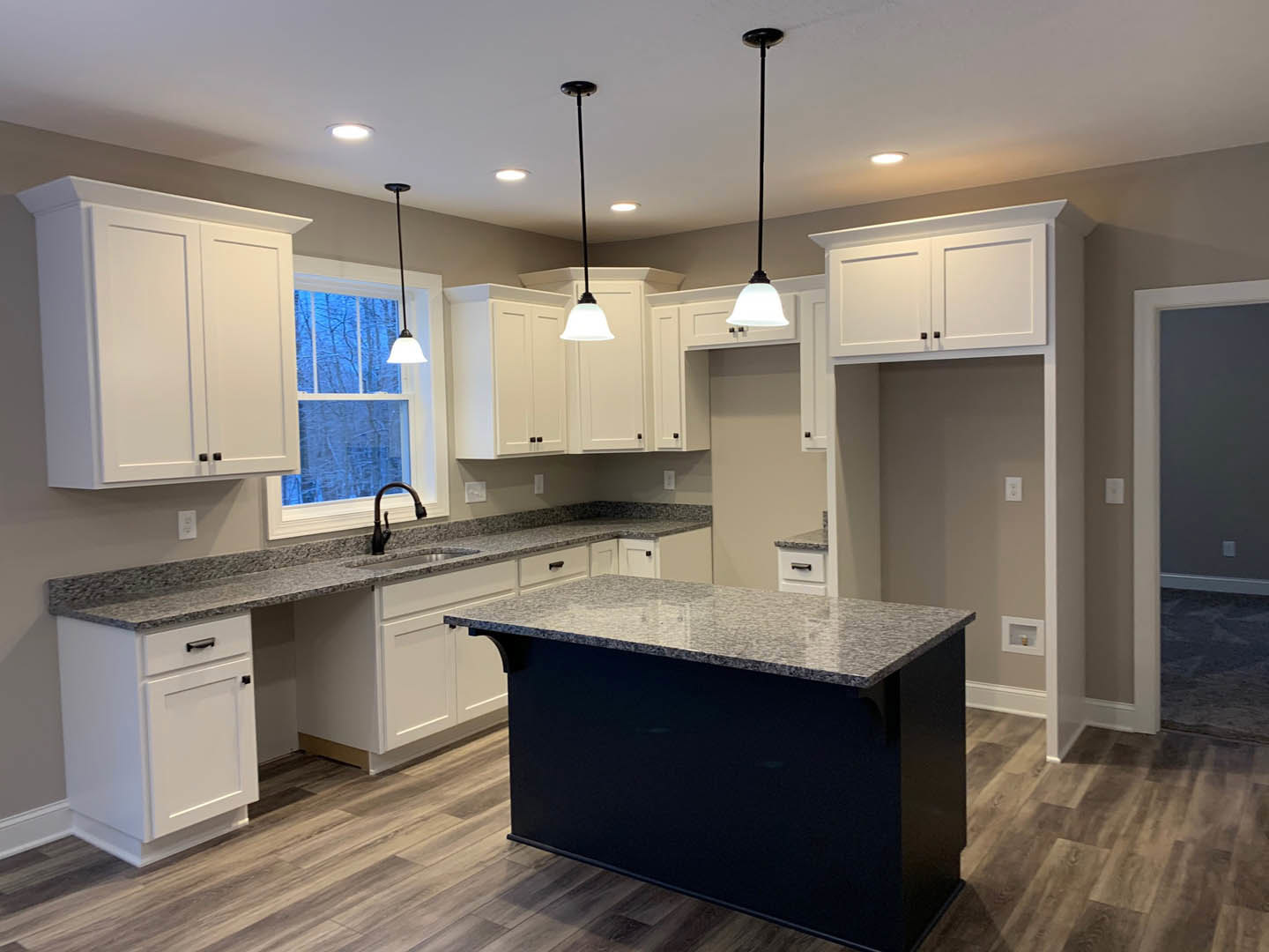 White shaker cabinets with black hardware, black kitchen island with waterfall countertop, stainless steel sink, light tile backsplash, recessed ceiling lights, hardwood flooring
