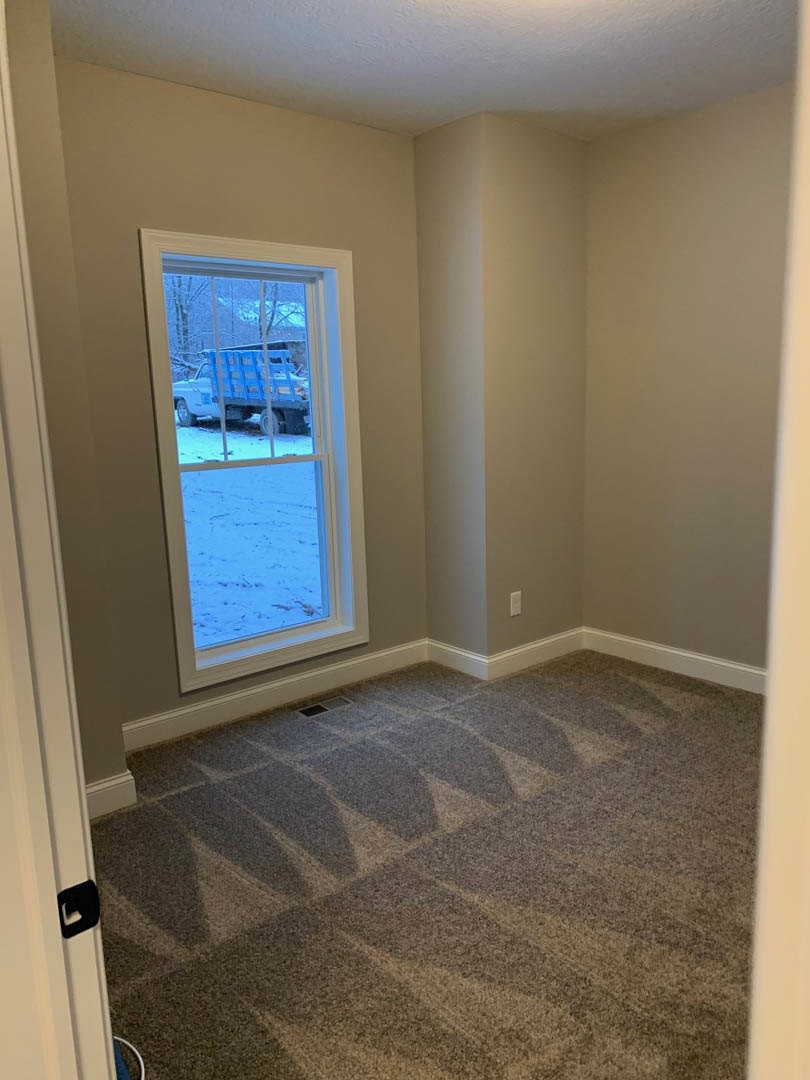 Carpeted bedroom with white walls, large window overlooking snowy field and blue truck with ladder