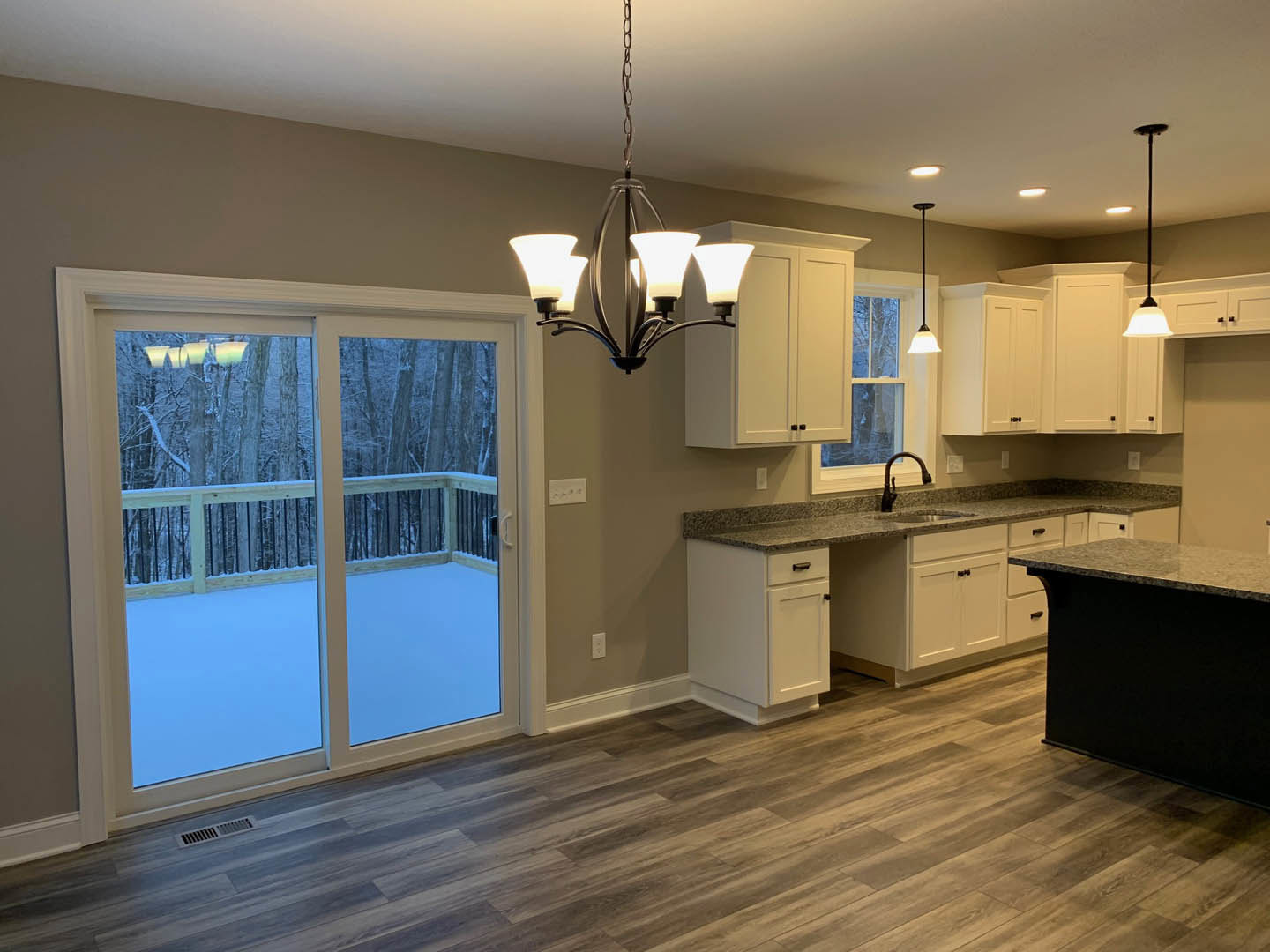 Modern kitchen featuring a black countertop, wood flooring, cabinetry, and a large sliding glass door opening to a snowy deck; chandelier and ceiling lights provide illumination.