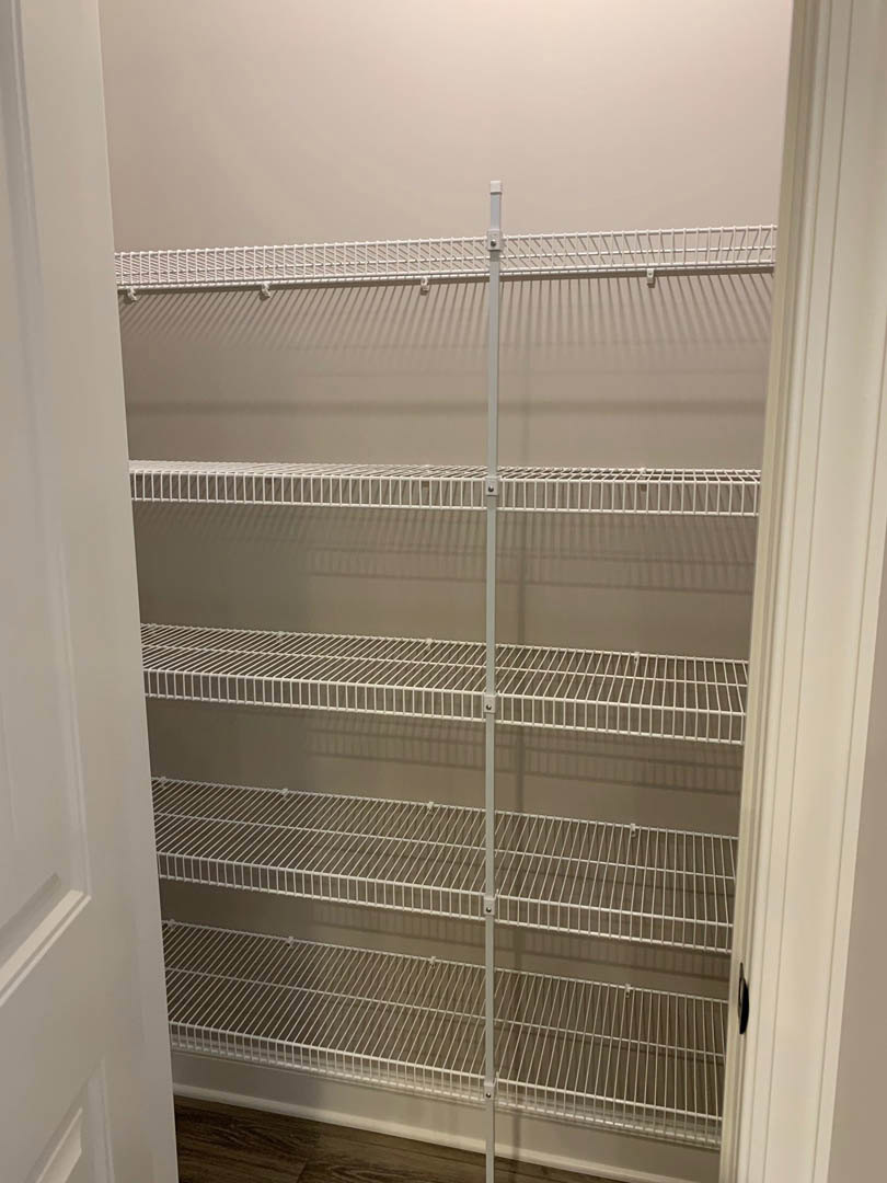 White wire shelves and metal hanging rod installed in a plaster-walled closet with natural light from a nearby window.