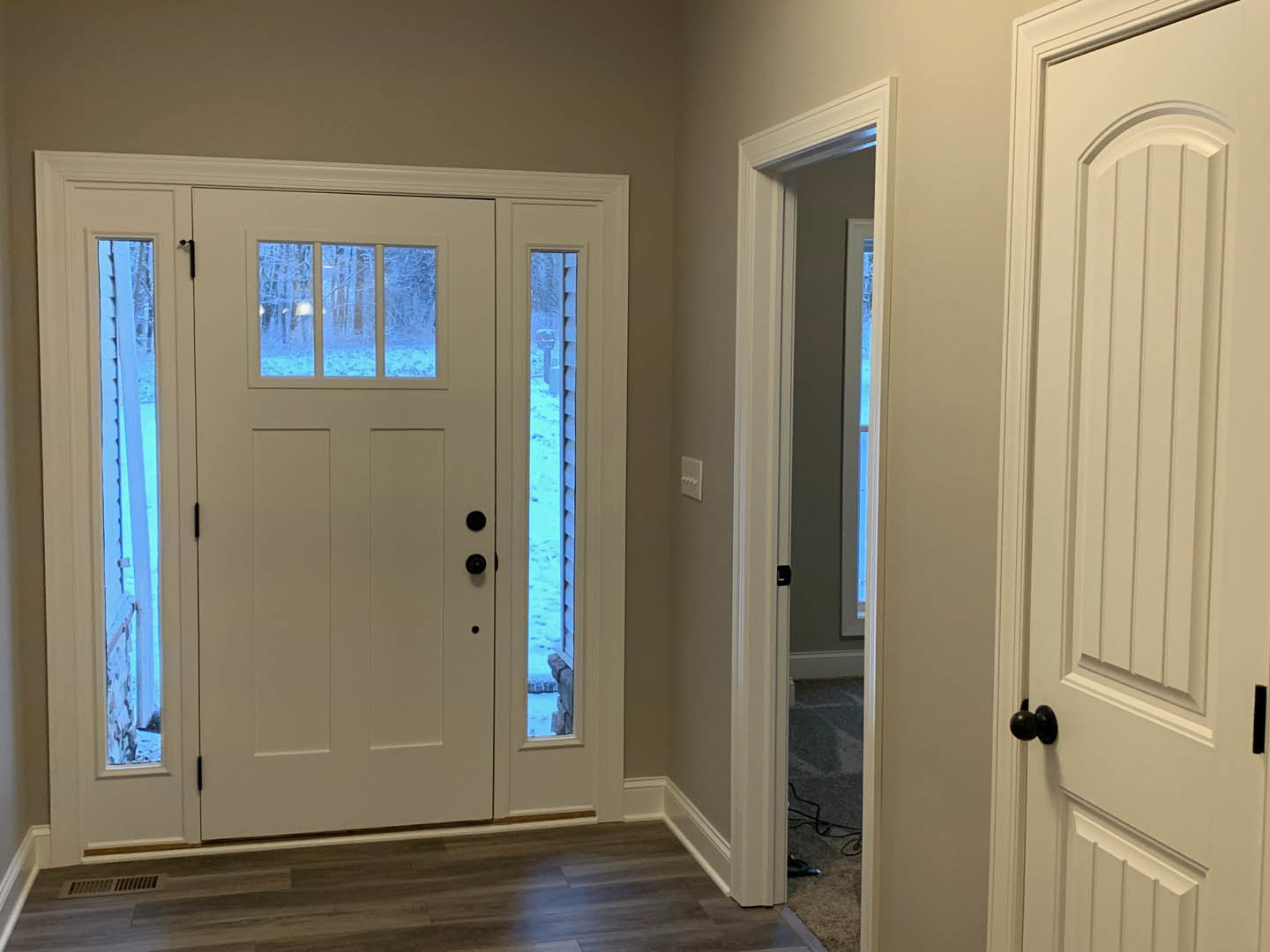 Hallway with white paneled doors, wood plank flooring, and a window showing snowy landscape
