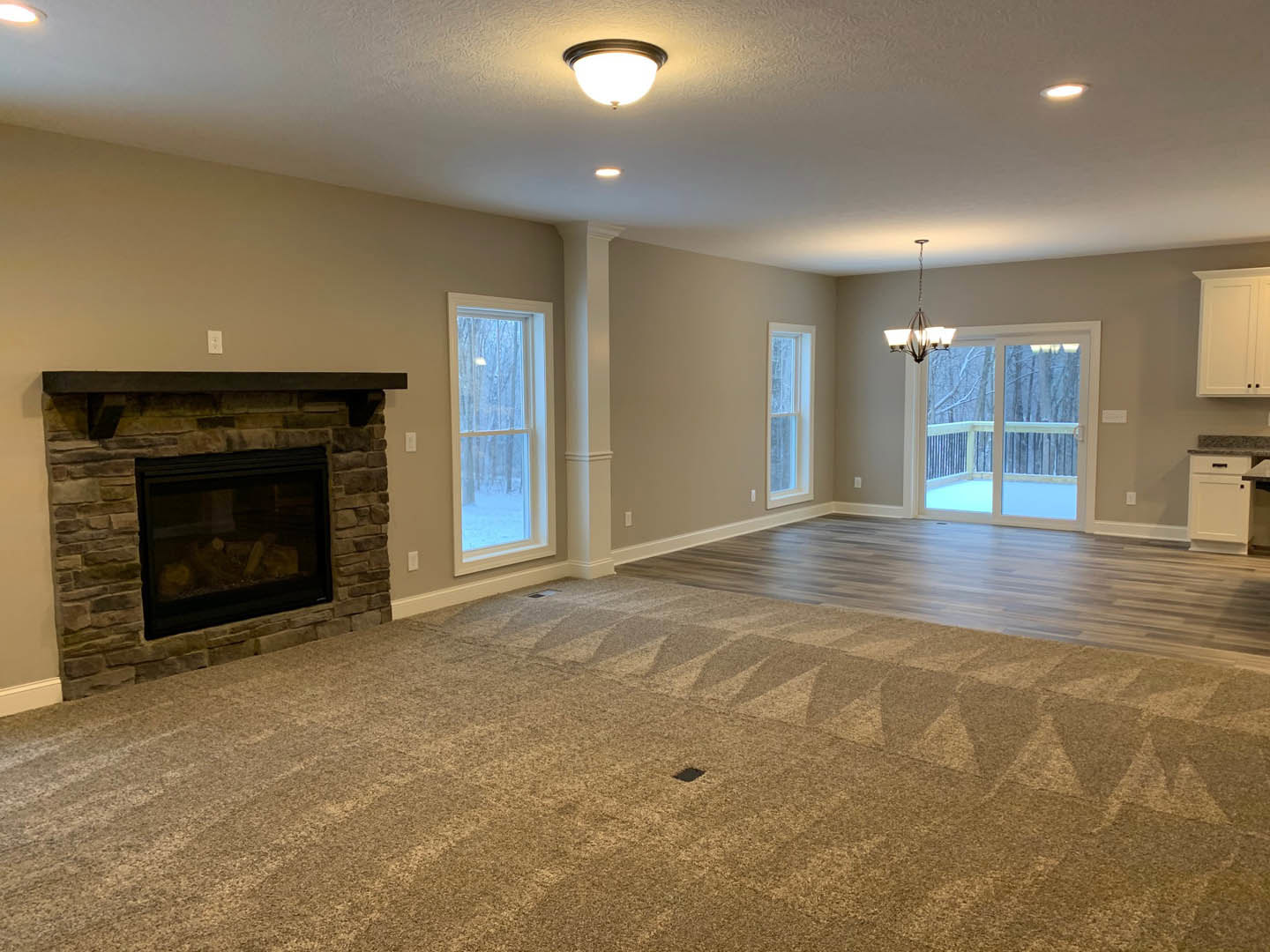 Living room with beige carpet flooring, black glass fireplace, white-framed window, and round ceiling light fixture