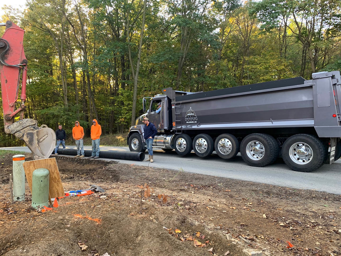 Modern custom home exterior with light stone facade, large windows, and landscaped front yard; group of people and a multi-axle truck parked on paved driveway, surrounded by mature