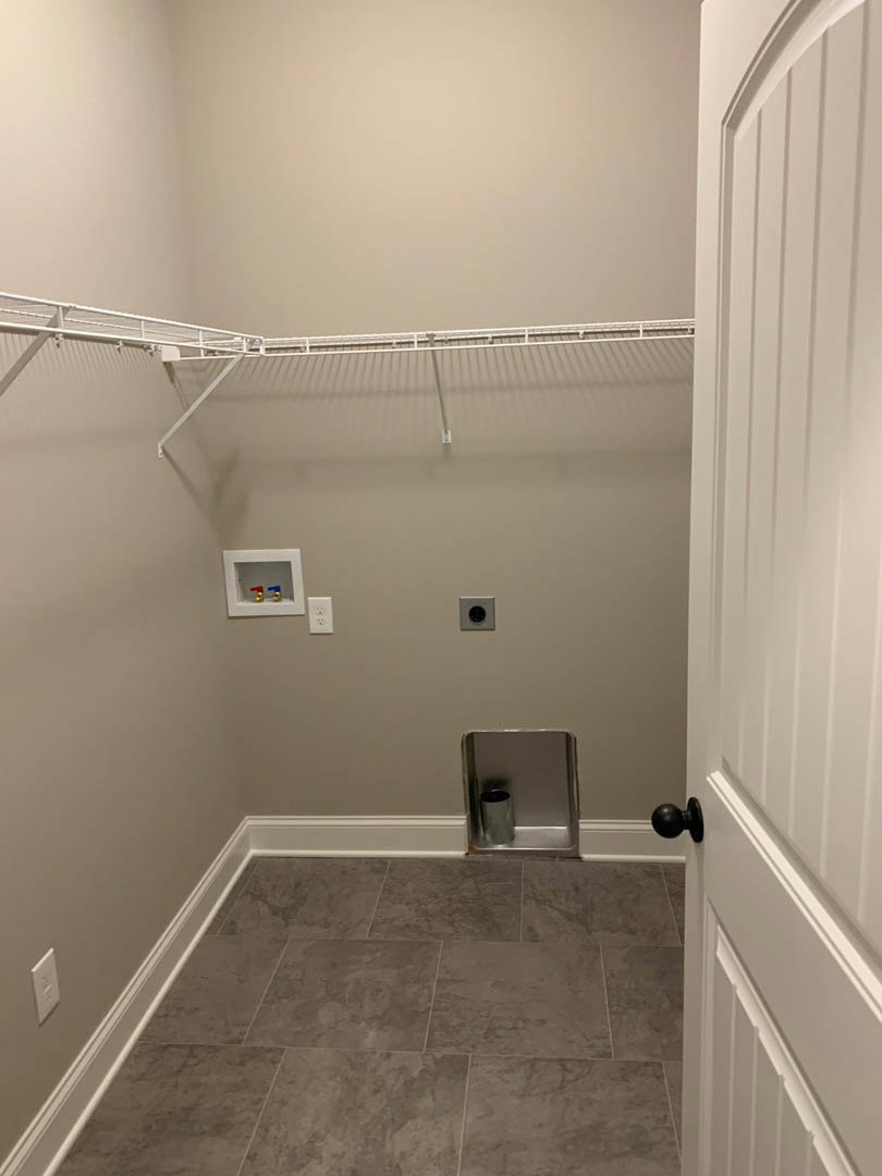 Closet with metal bin on shelving, silver can, grey tile floor with white baseboard, white-framed square display holding red and blue gun-shaped object, black door knob on white
