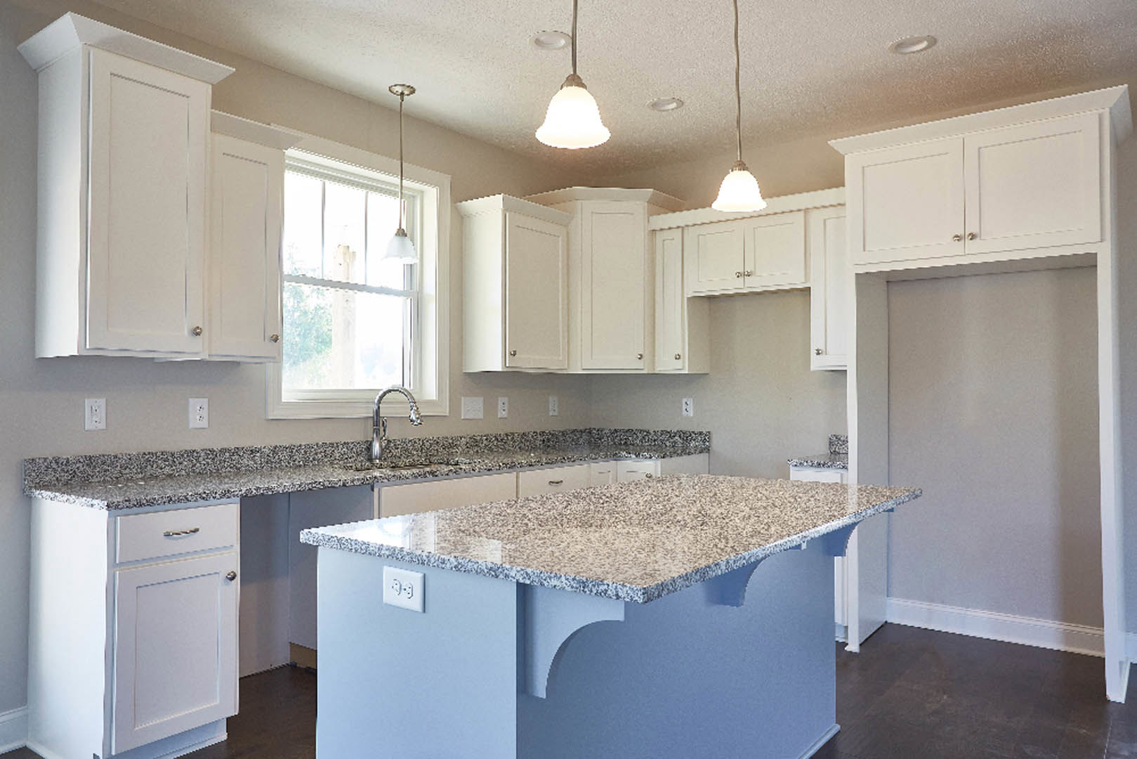 Granite countertops, white shaker cabinets, stainless steel sink, blue accent wall, sunlight streaming through window