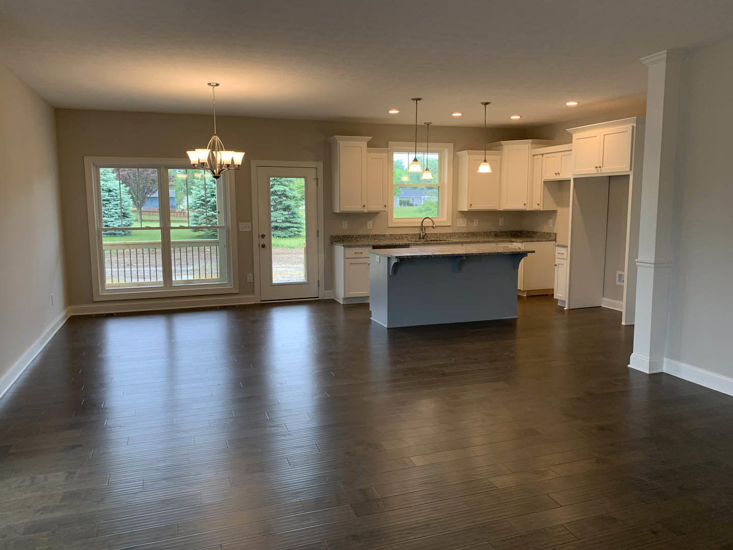 Open-concept kitchen and dining area featuring a large central island with white cabinetry, hardwood floors, glass-paneled door, modern chandelier, and expansive window overlooking