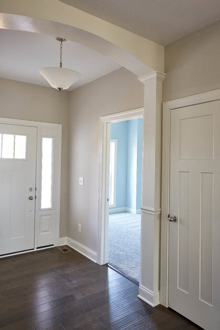 Hallway with white paneled doors, brushed silver knobs, dark wood flooring with a floor vent, and a modern ceiling light fixture