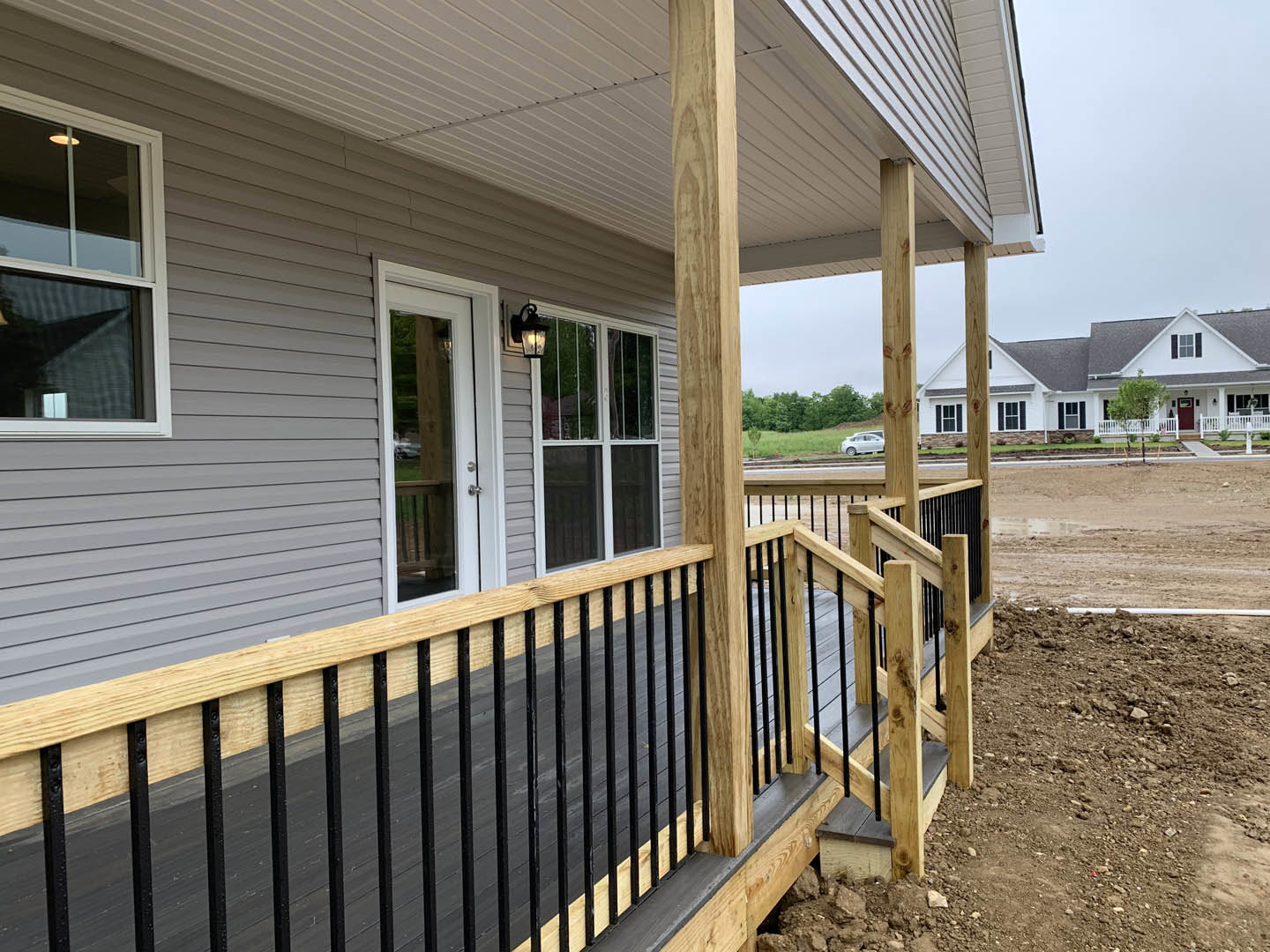 Front porch with white wooden railing, glass-paneled door, large window, and light-colored siding