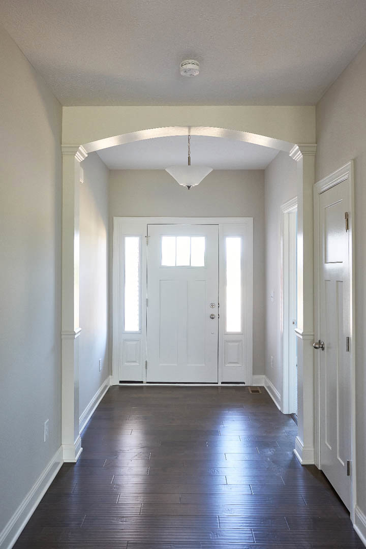 Hallway with dark wood flooring, white walls, and a white door featuring a window panel