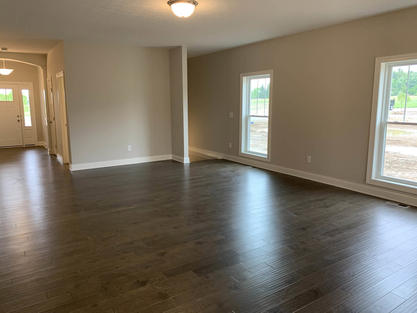 Empty room with light wood flooring, white walls, large window overlooking grassy yard, ceiling-mounted light fixture
