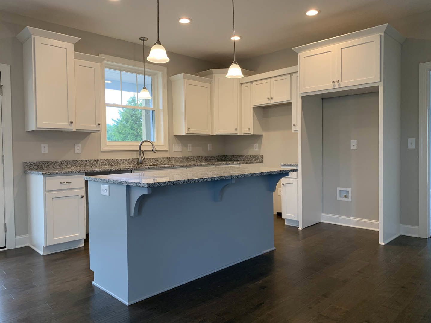 Marble kitchen island with waterfall edge, white shaker cabinets, gold pendant light, stainless steel faucet over undermount sink, wide window letting in natural light, white door