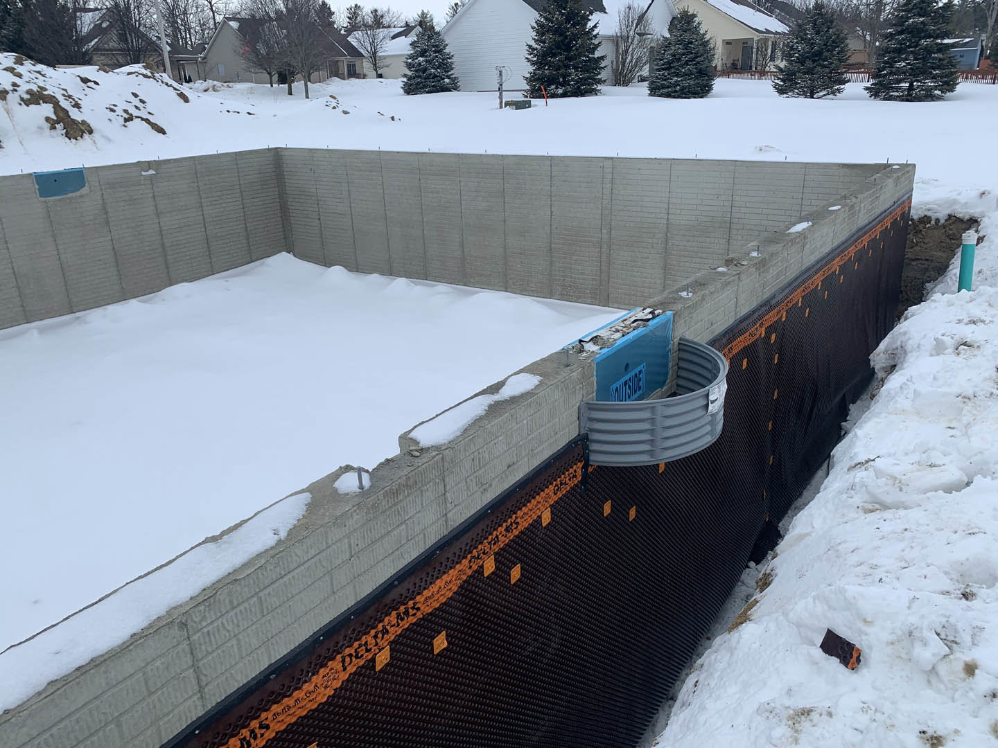 Concrete foundation surrounded by snow, bare trees in background, winter landscape