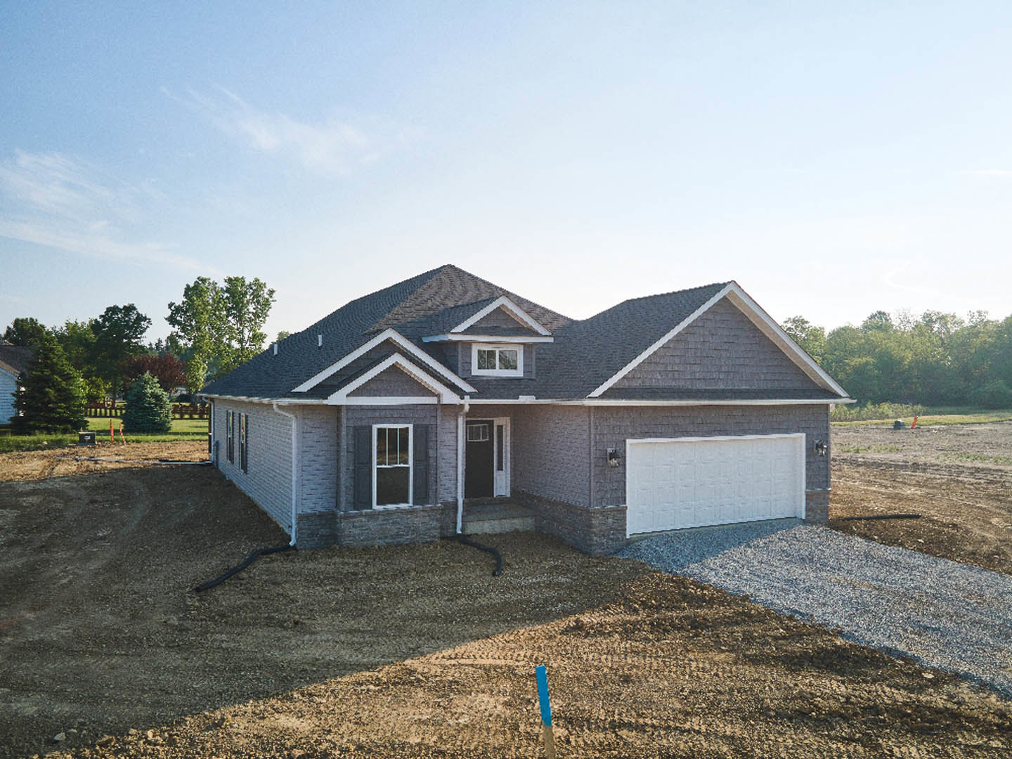 Modern home under construction featuring a paved driveway, attached garage with black door and white frame, white exterior walls, large window with white trim, red flag, and a
