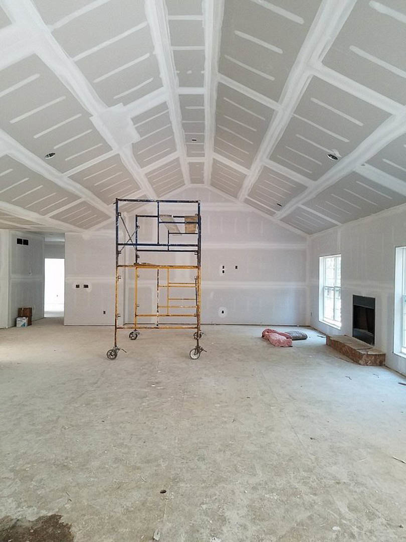 Metal scaffolding stands on a concrete floor in an empty room with white-painted ceiling, white-framed window, and a brown rectangular object resting on a white surface.