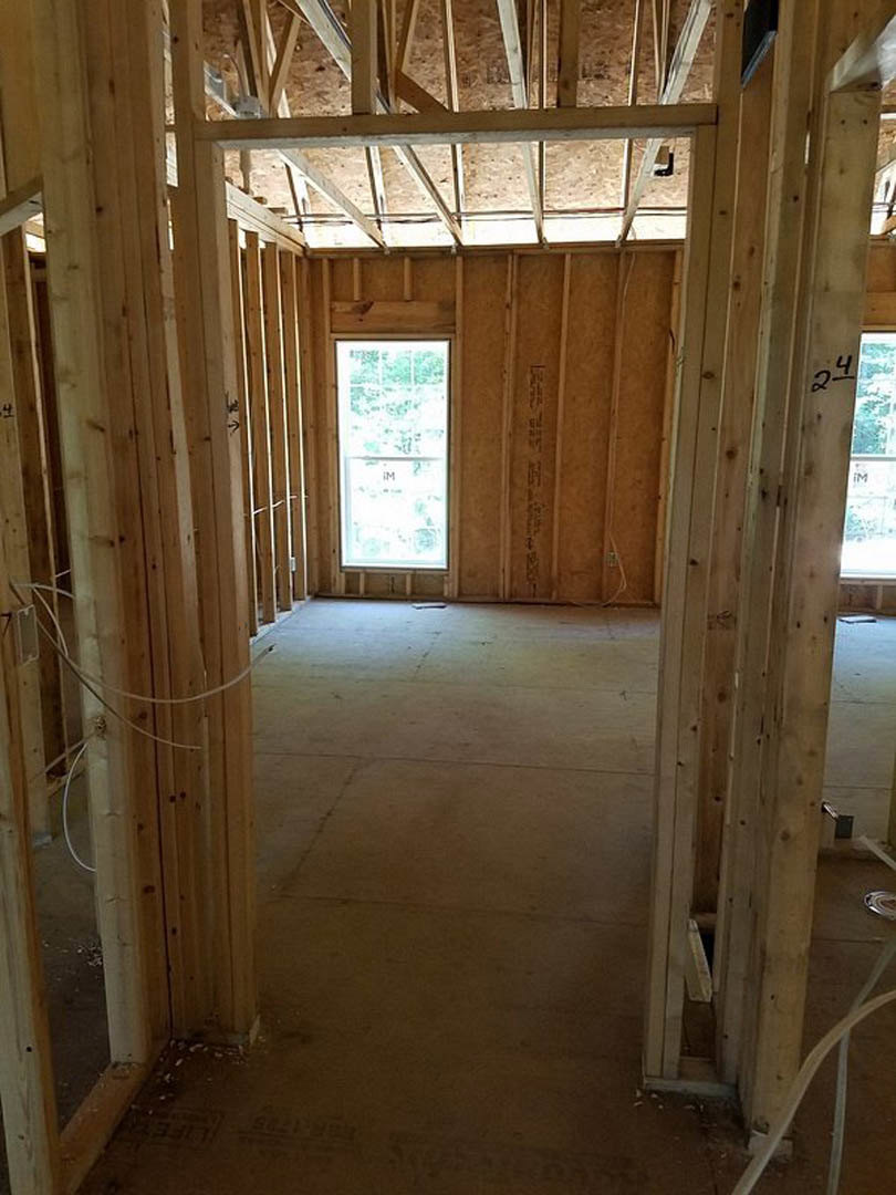 Unfinished room with exposed wood framing, roof trusses, wall insulation, and a window set in a white wall