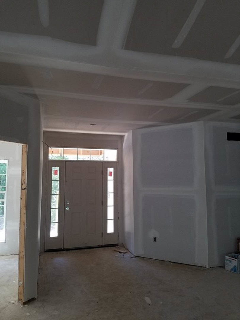Grey door with glass panels set in a white wall, light switch visible beside the door, dirty floor with scattered debris, ceiling and plaster finishes, small white box with blue