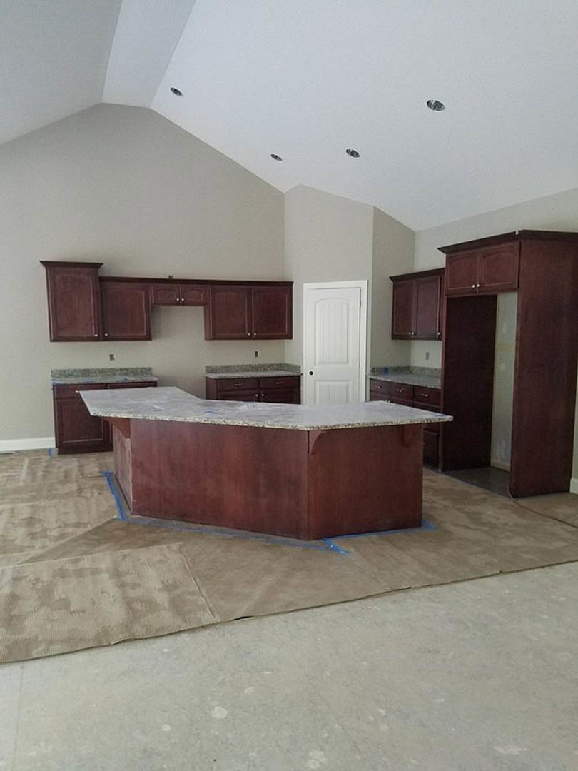 Marble countertop with white cabinets, stainless steel sink, black cabinet handles, and light wood flooring in a modern kitchen.