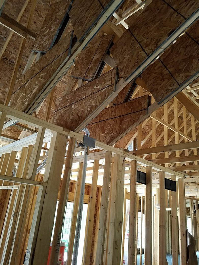 Exposed wood framing and ceiling beams inside a house under construction, with visible lumber, insulation, and construction materials