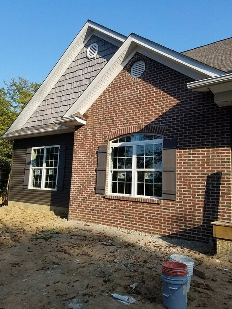 Red brick exterior with multi-pane window, white trim, metal vent, and blue plastic bucket on ground