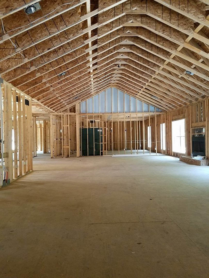 Living room with exposed wood beam ceiling, stone fireplace, hardwood floors, and large windows with white trim