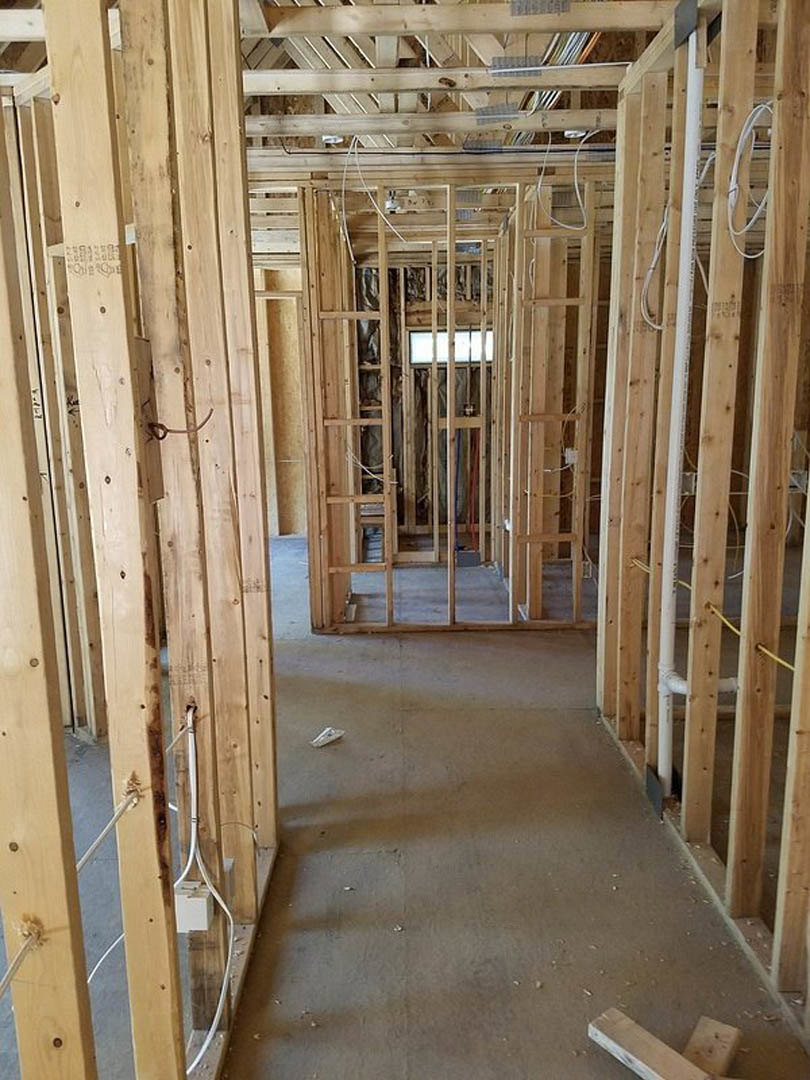 Room with exposed wood ceiling beams, unfinished wood plank walls, large window, and concrete floor in residential construction.
