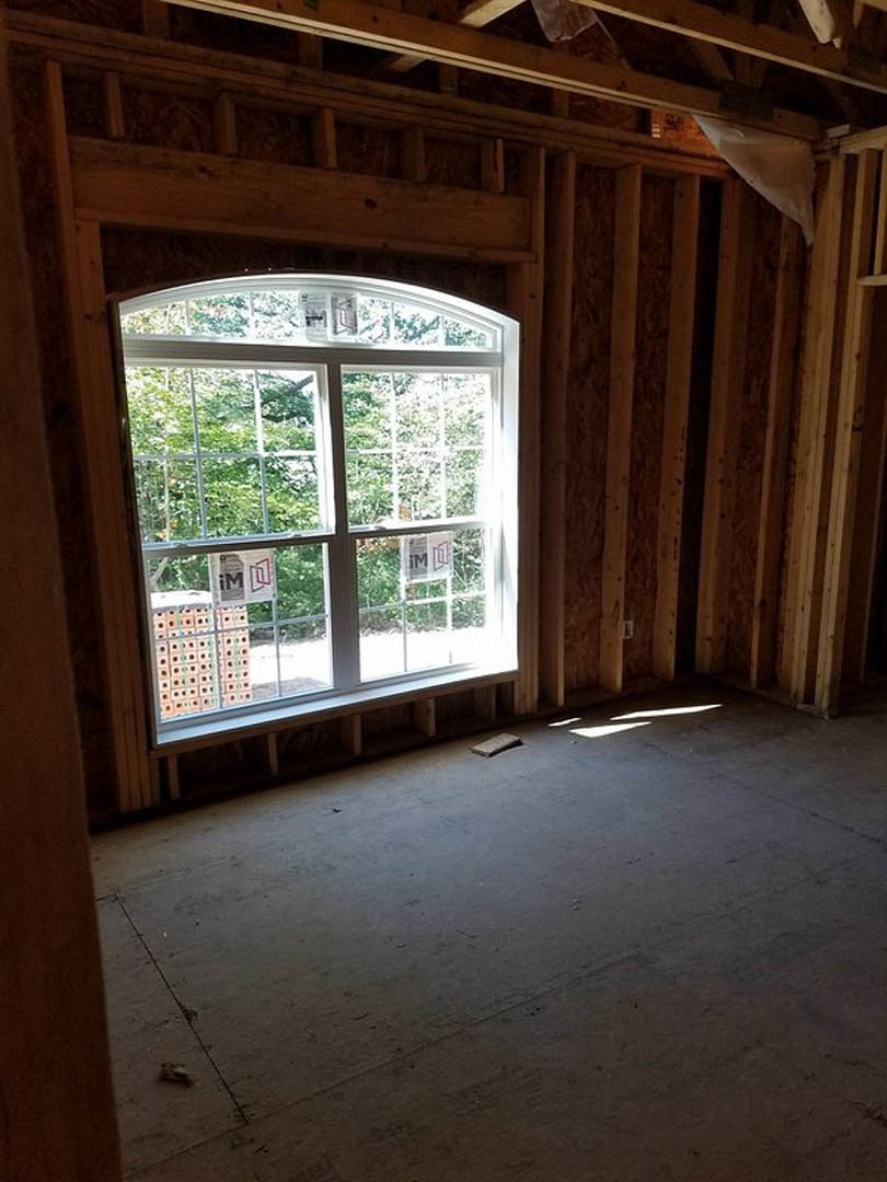 Room with large white-framed window, exposed concrete floor, and visible wood beams