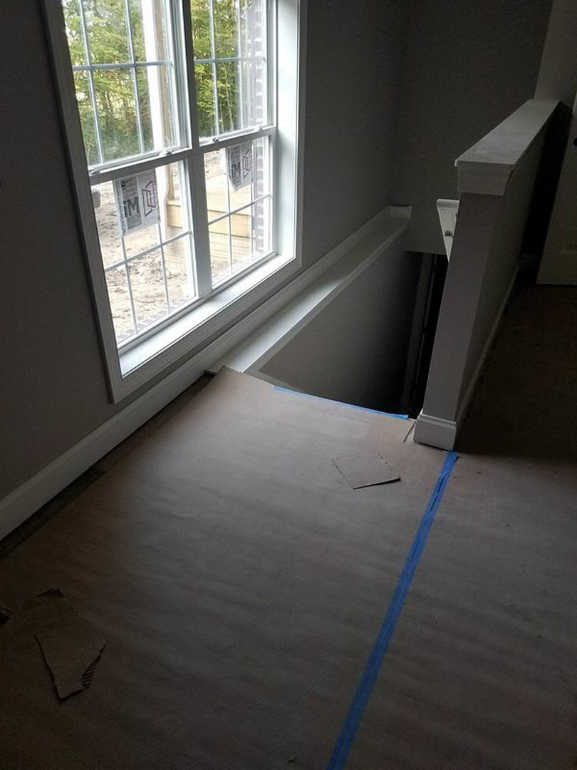 White-framed window set in a white plaster wall, white door, concrete floor with blue tape, cardboard floor covering, close-up of tile and laminate flooring