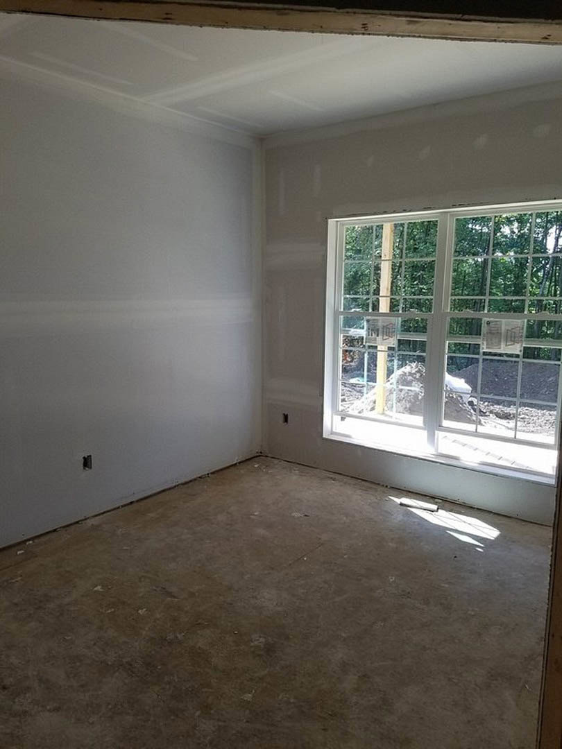 Sunlit room with plaster walls, large windows, light wood flooring, and a white object near the baseboard