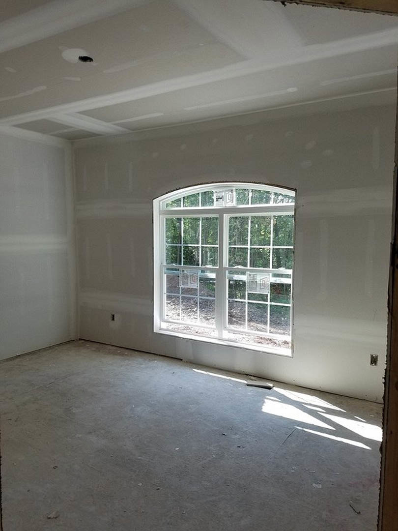 Sunlit room featuring a large window, smooth concrete floor, white plaster walls, and minimalist ceiling.
