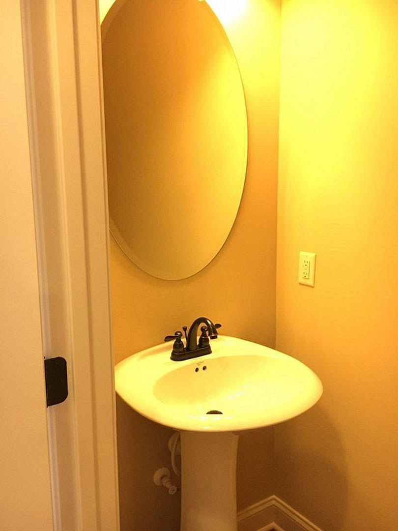 White porcelain sink with chrome faucet beneath a rectangular wall-mounted mirror, set against light-colored tile backsplash in a modern bathroom.